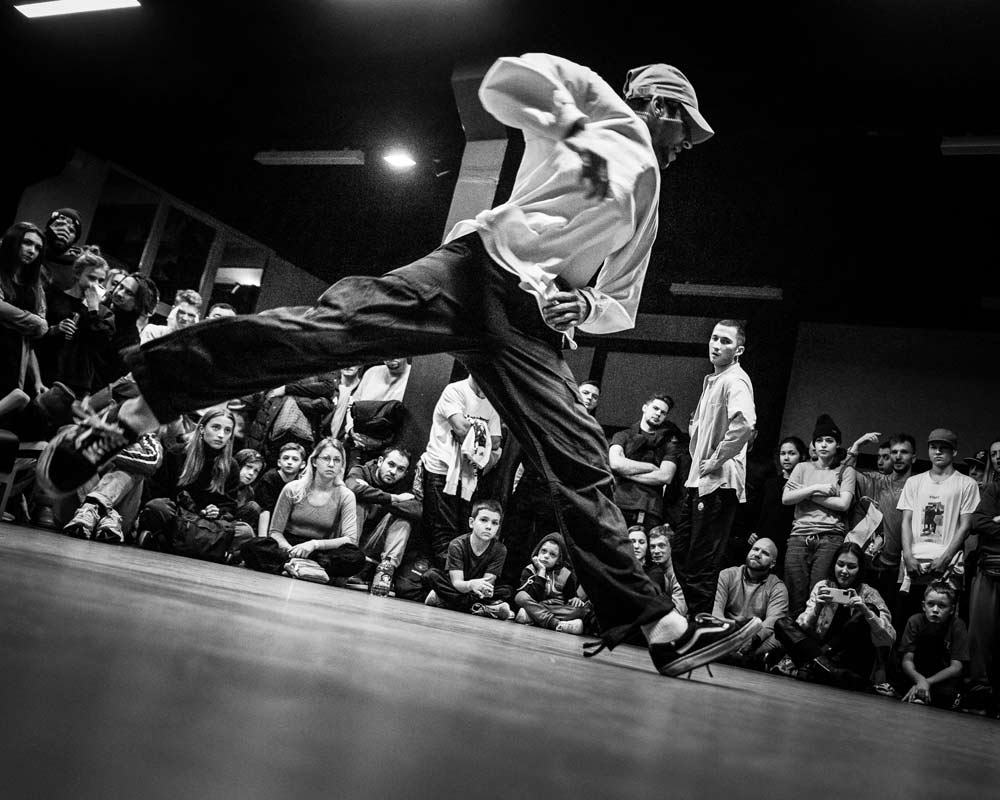 Breakdancer macht eine Figur, im Hintergrund sitzen und stehen Zuschauer.