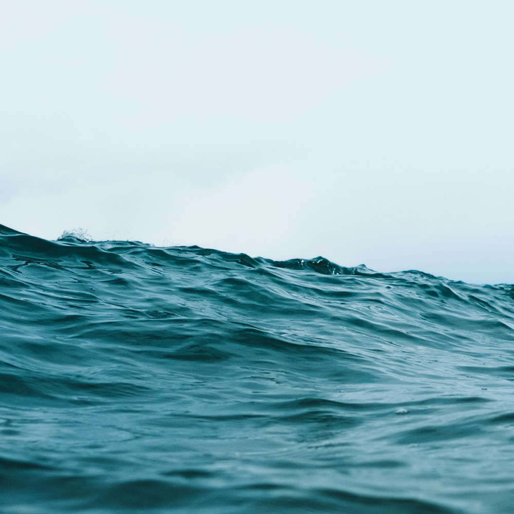 Ausschnitt einer Großaufnahme des offenen Meerer. Welliges Wasser, grünlich blau in der Farbe mit Lichtreflexionen.