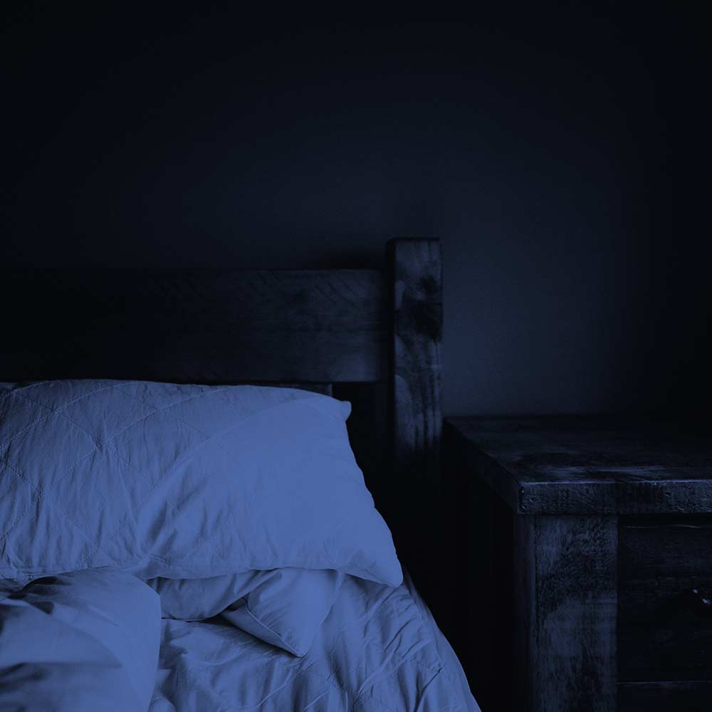 Holzbett mit weißen Bettbezügen in nächtliches blaues Licht getaucht